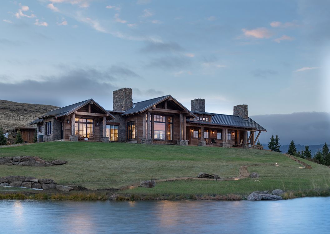 A large house is sitting on top of a hill next to a lake.