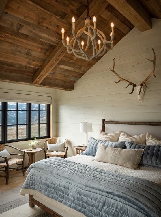 A bedroom with a bed a chandelier and antlers on the wall