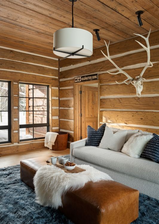 A living room in a log cabin with a couch and antlers on the wall.