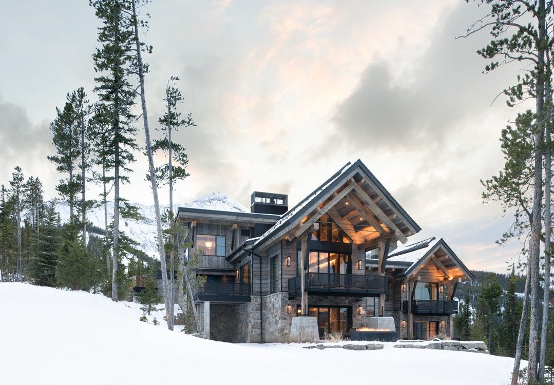 A large house is sitting on top of a snow covered hill surrounded by trees.
