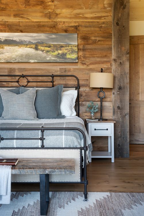 A bedroom with a bed , nightstand , lamp and wooden wall.