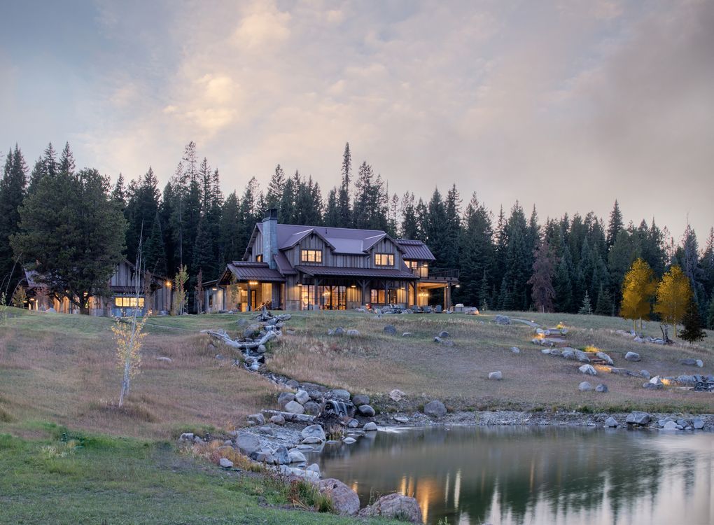 A large house is sitting on top of a hill next to a lake surrounded by trees.