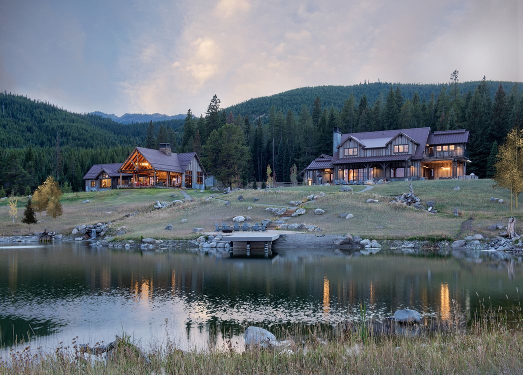 A large house is sitting on top of a hill next to a lake.