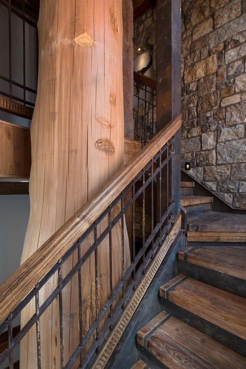 A wooden staircase with a metal railing and a stone wall