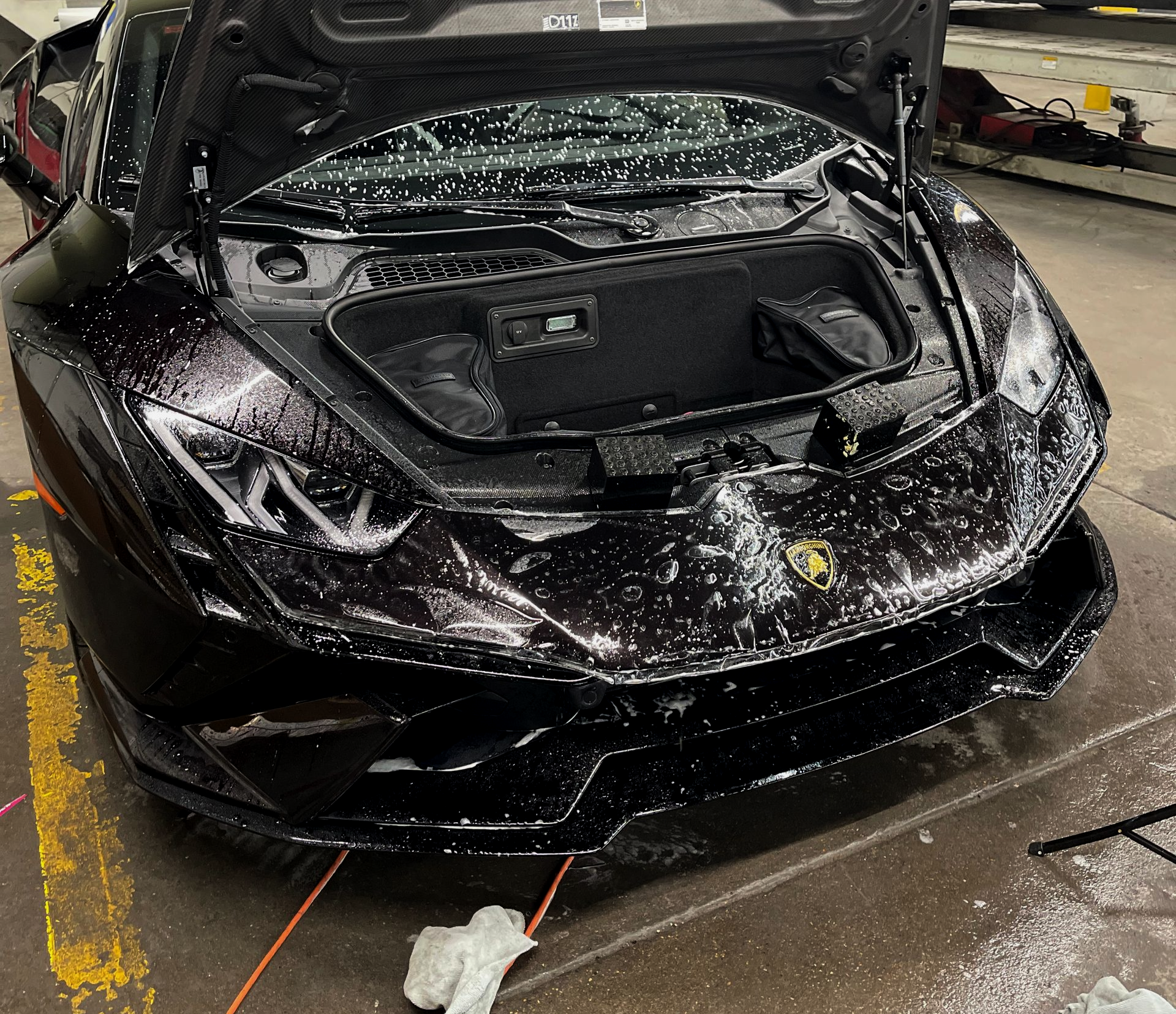 Damaged black Lamborghini with the hood open, inside a garage.