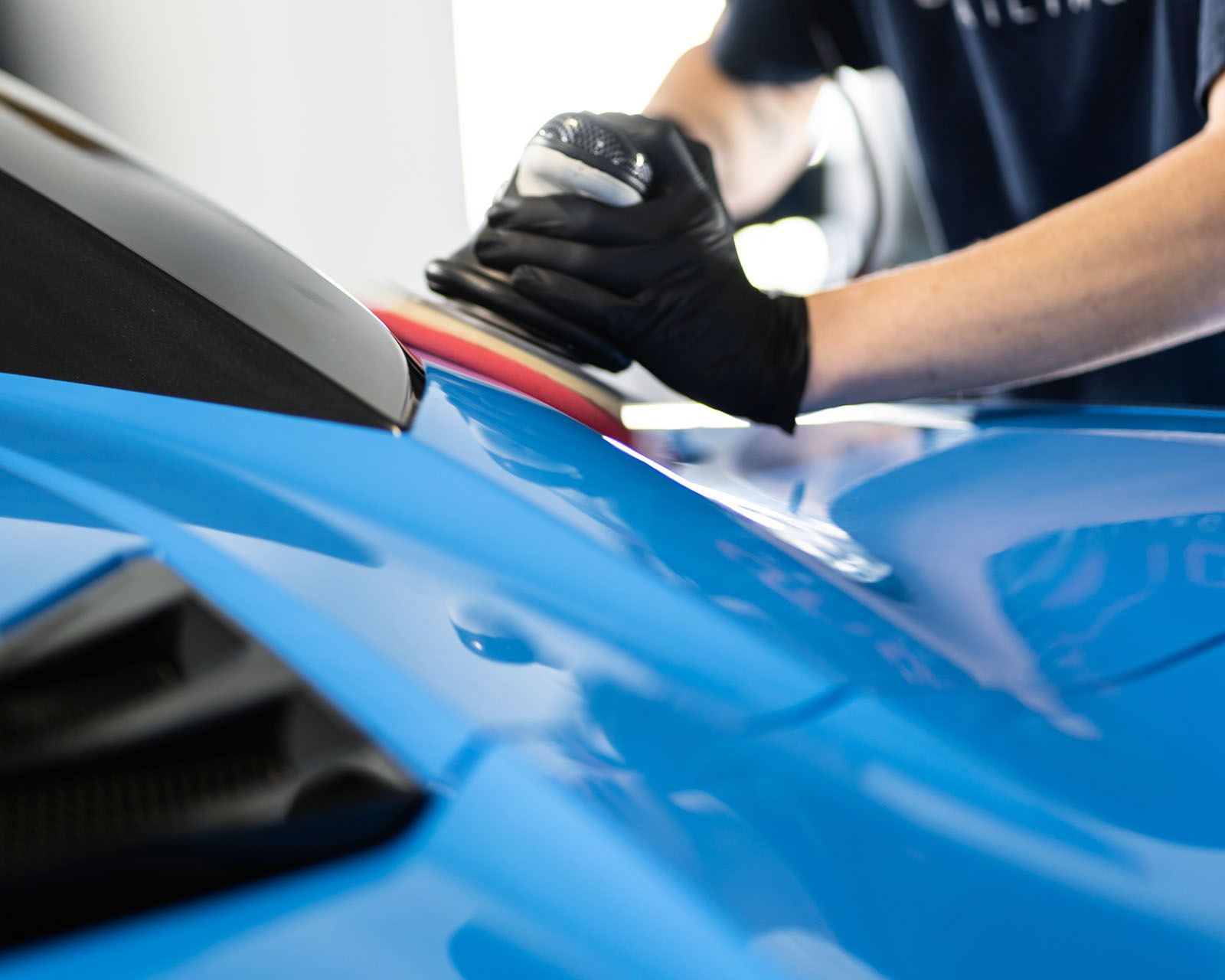 Person in black gloves polishing a bright blue car with a machine.