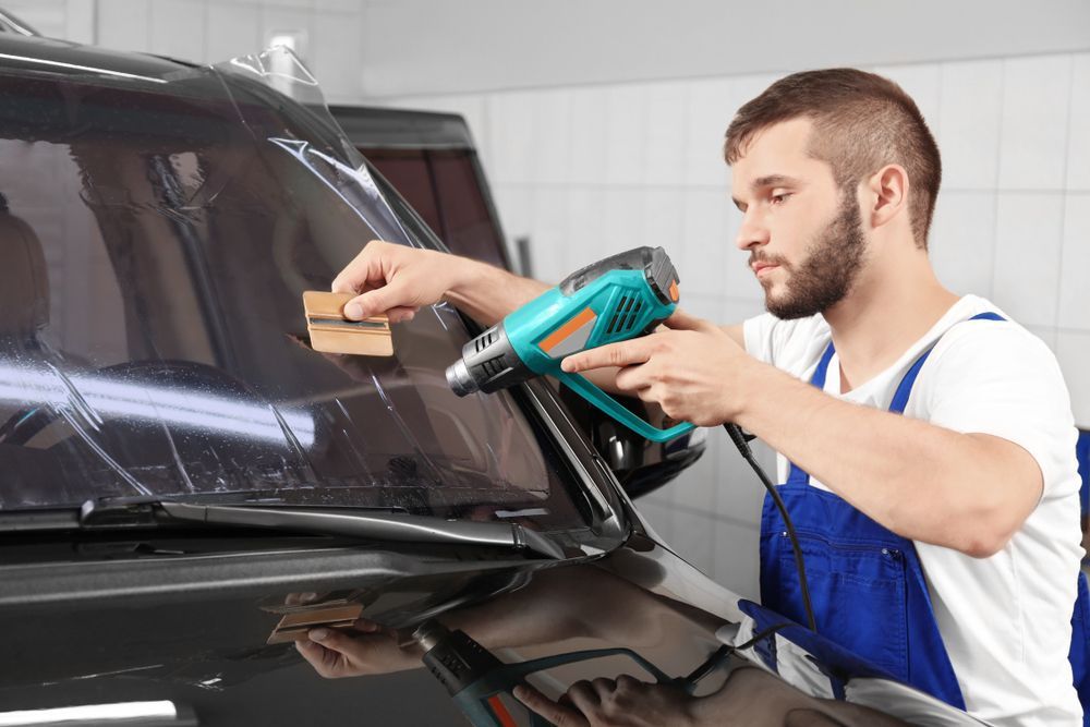 A Man Is Applying Tinted Glass To A Car Window — Eurobodalla Windscreens in Moruya, NSW