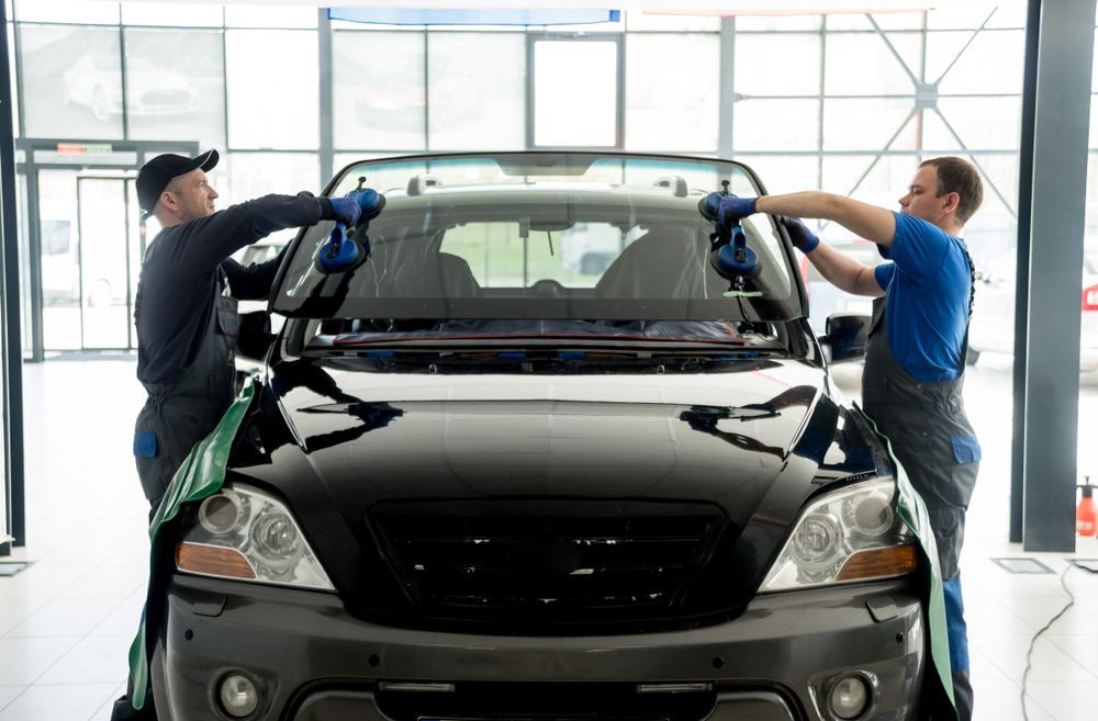 Two Men Are Installing A Windshield On A Car In A Garage — Eurobodalla Windscreens in Narooma, NSW