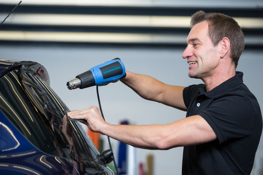 A Man Using a Heat gun to Apply or Adjust a Film on a car Window — Eurobodalla Windscreens in Batemans Bay, NSW