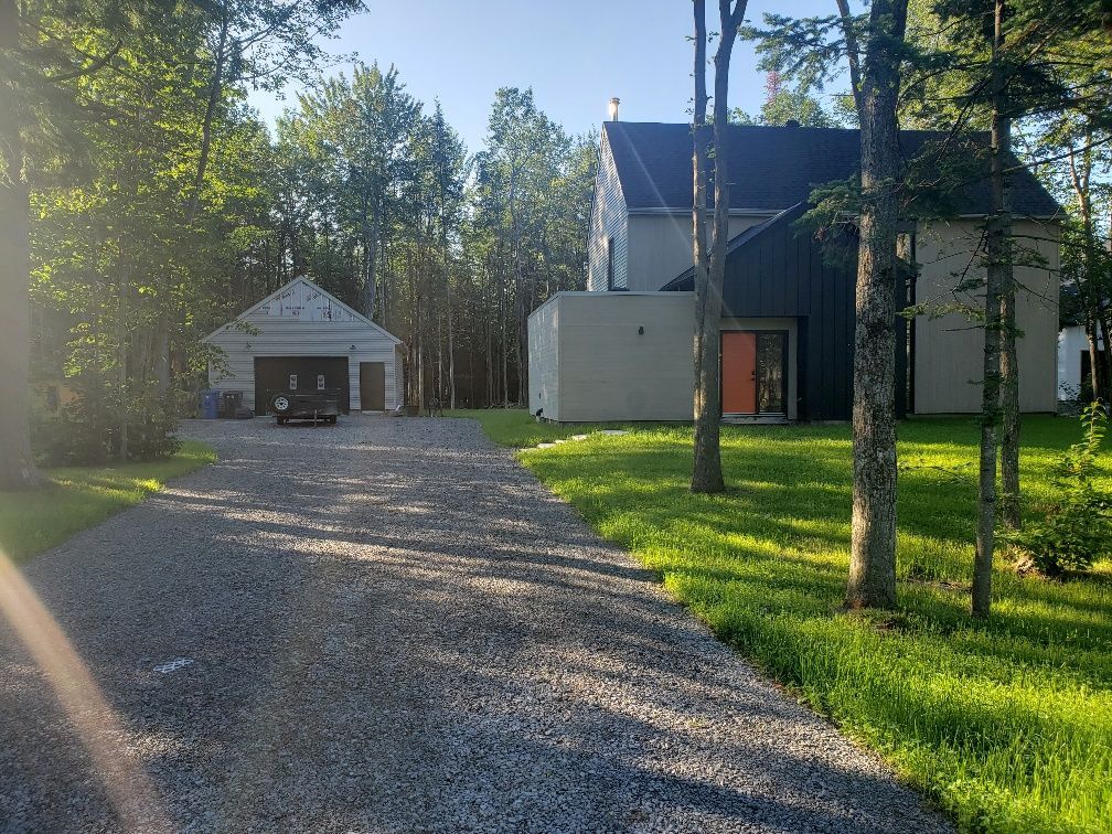 Une allée de gravier menant à une grande maison entourée d'arbres.