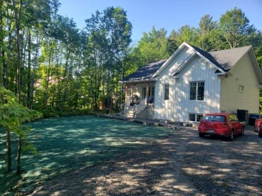 Une maison blanche avec une voiture rouge garée devant.