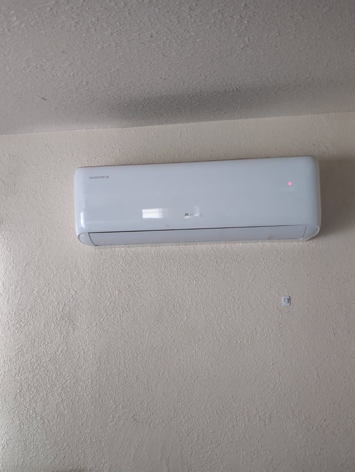 Wall-mounted white air conditioner on a beige wall near the ceiling.