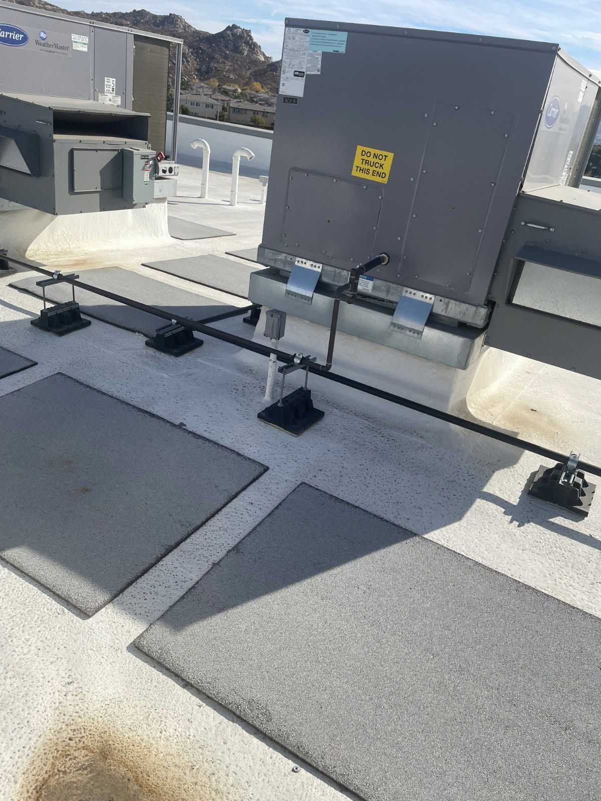 Rooftop HVAC units and ventilation pipes on a flat commercial roof under bright sun.