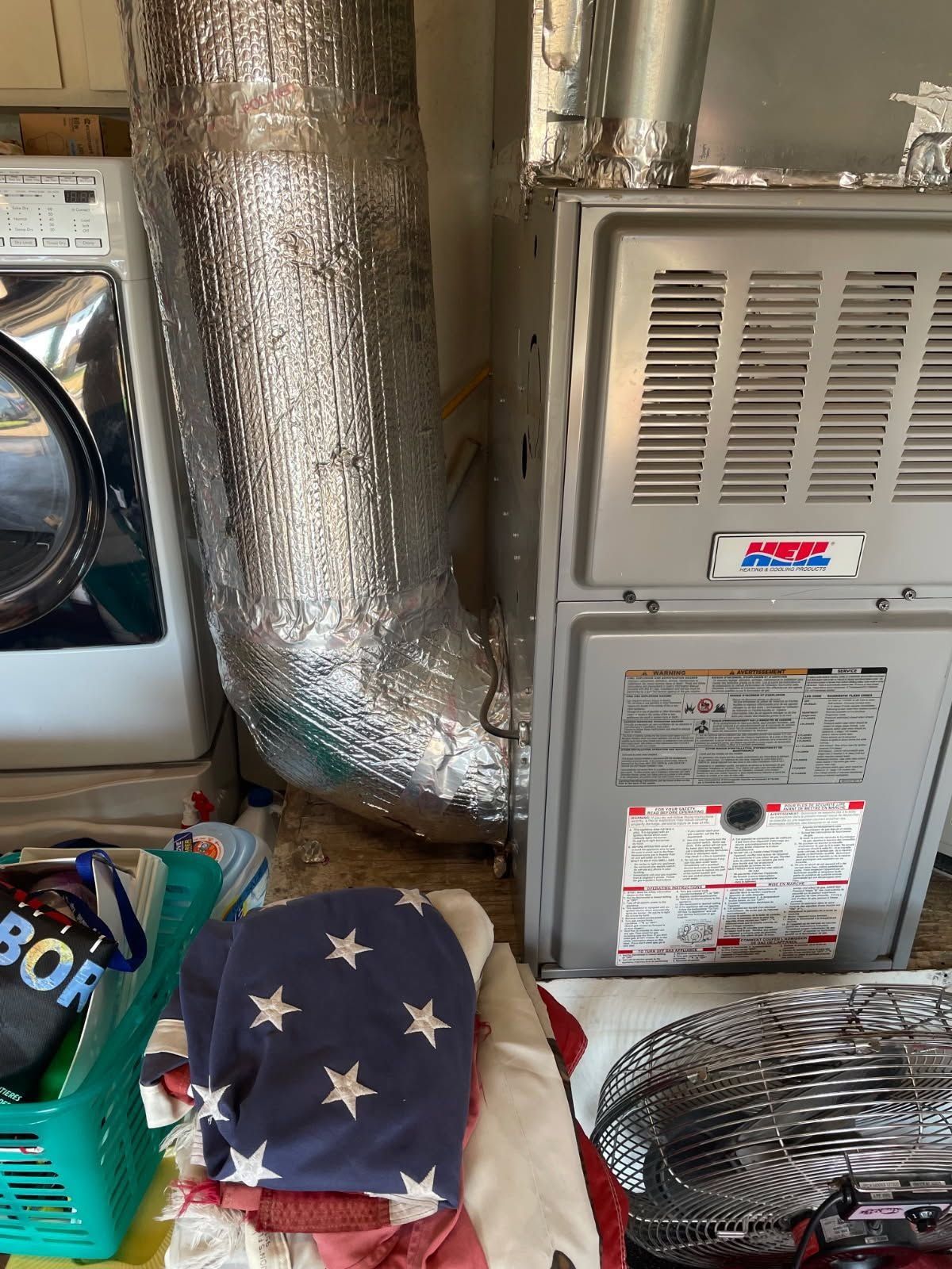Basement utility area with wrapped ductwork, furnace, dryer, fan, and folded American flag blanket