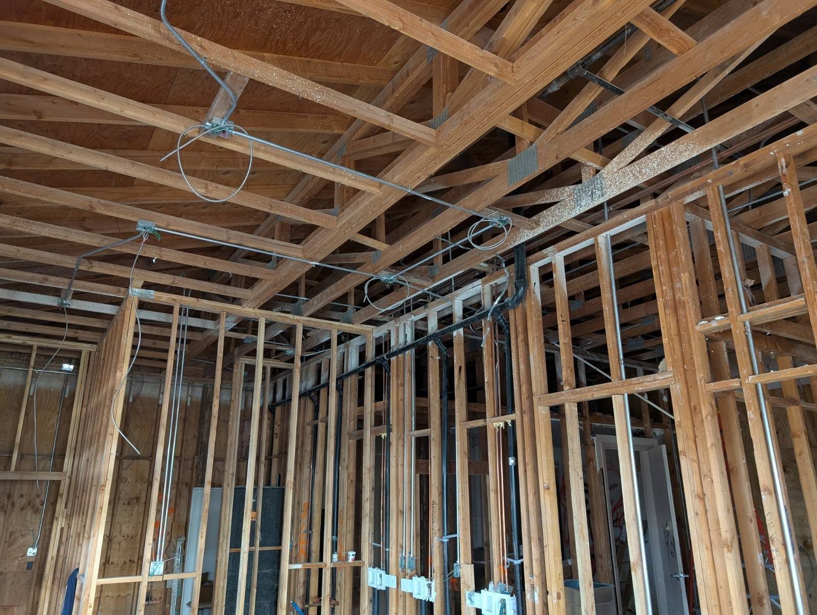 Wood-framed room under construction with exposed studs, ceiling joists, and blue electrical wiring.