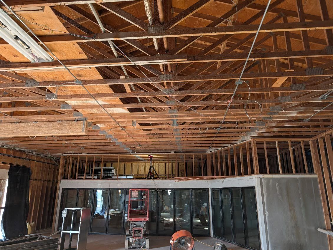 Exposed wooden ceiling framing in an unfinished room with a worker in an orange hard hat below