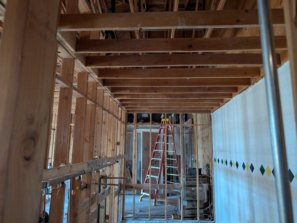 Unfinished hallway with exposed wood framing, blue drywall, and a ladder at the far end