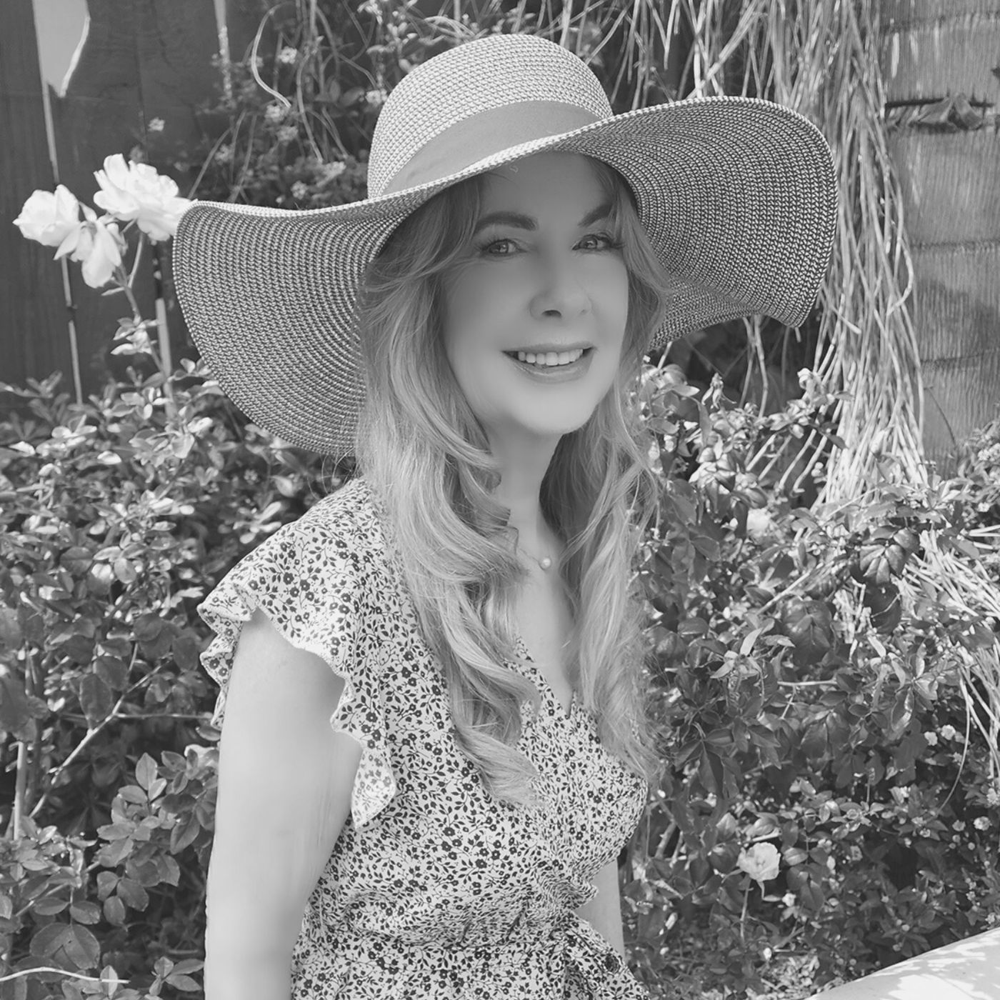A woman wearing a hat and a dress is smiling in a black and white photo.