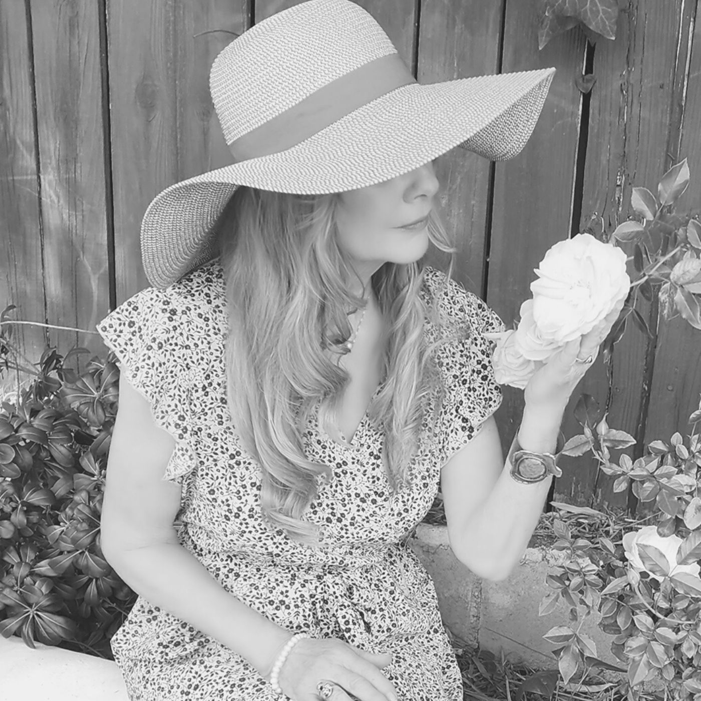A woman wearing a straw hat is smelling a flower.