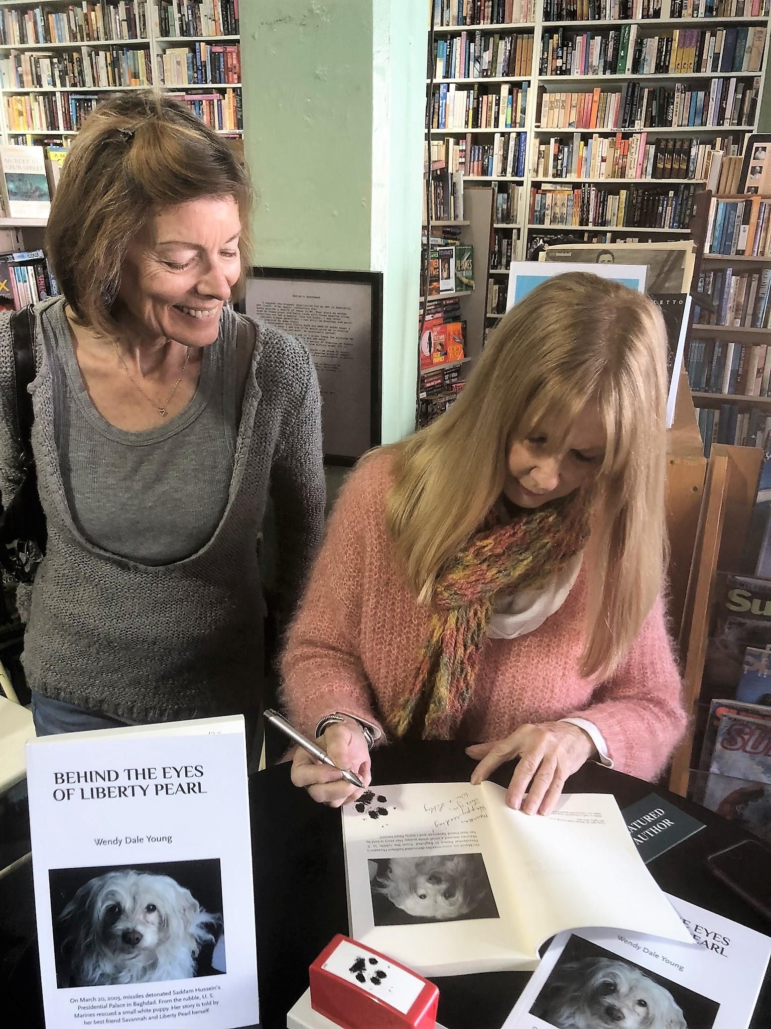 Two women are sitting at a table signing a book