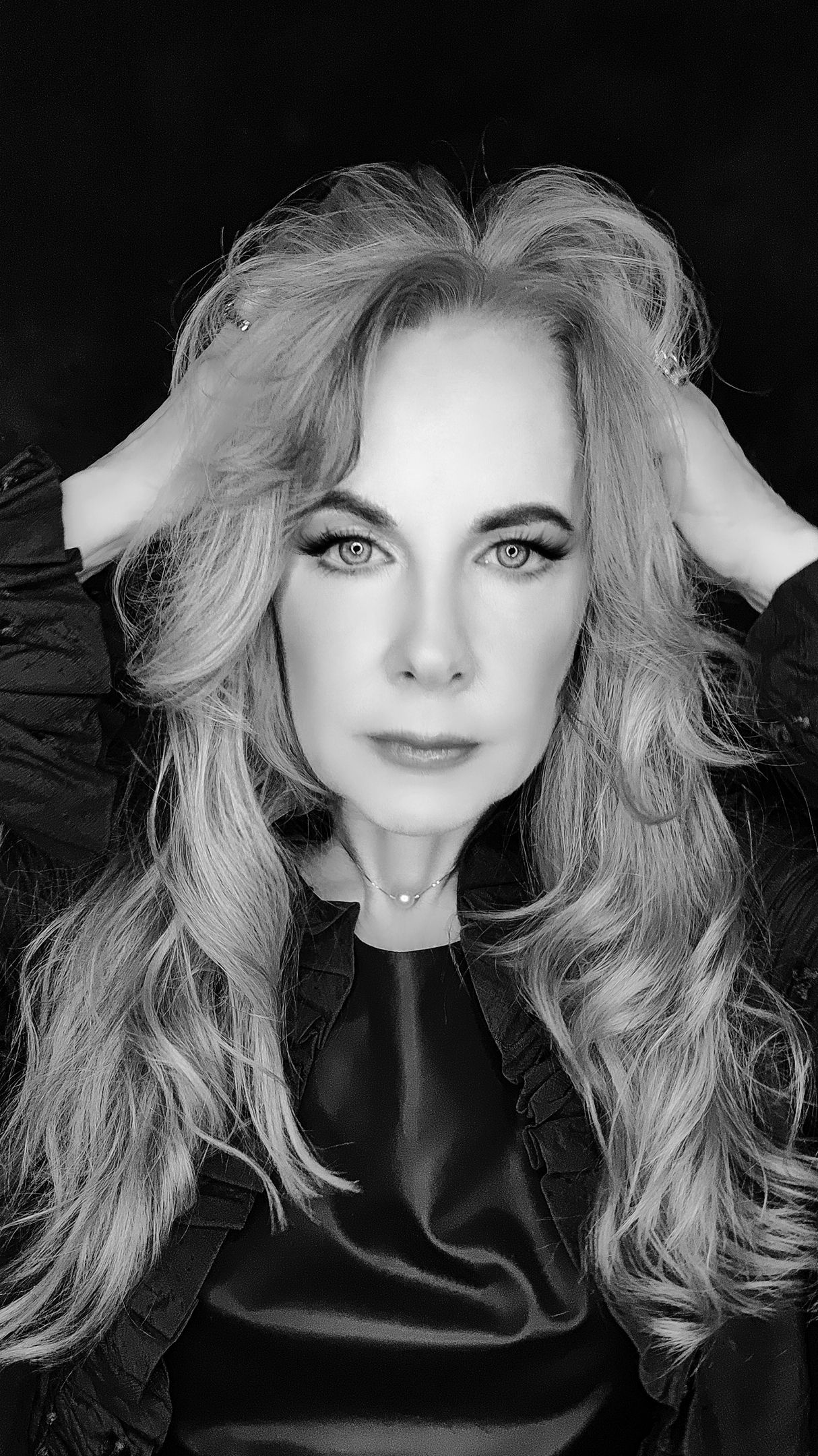 A black and white photo of a woman with long hair holding her hair.