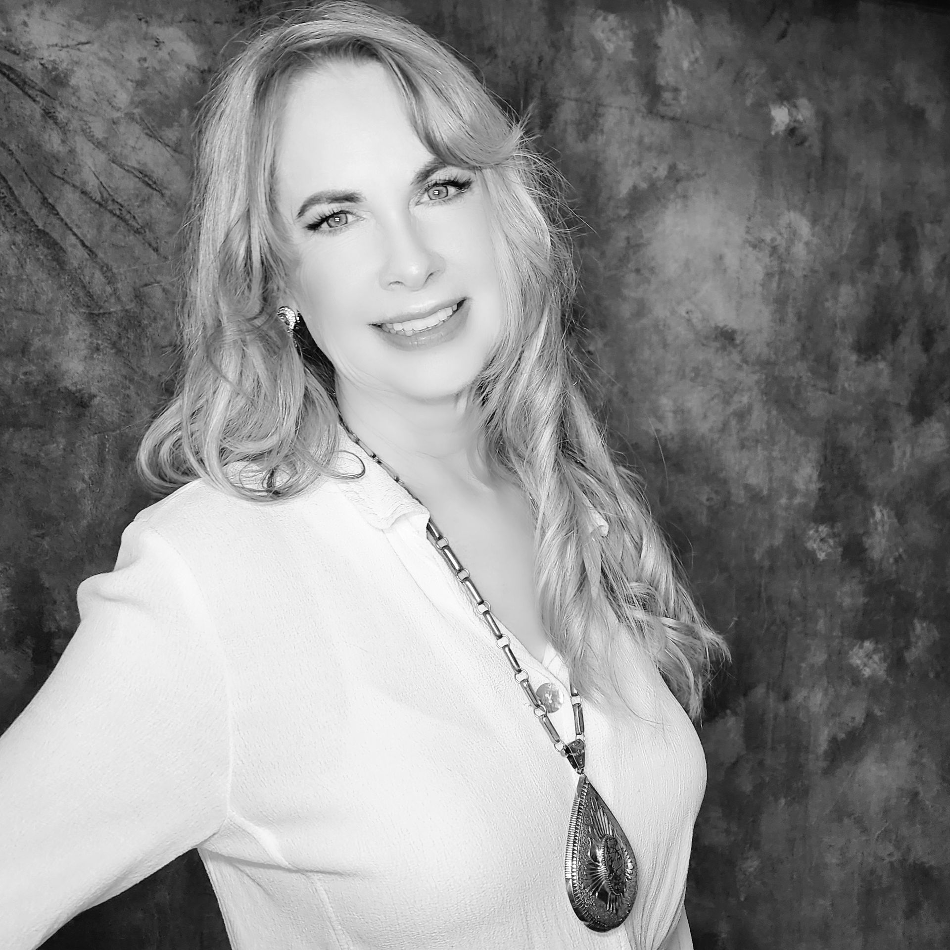A woman wearing a white shirt and a necklace is smiling in a black and white photo.