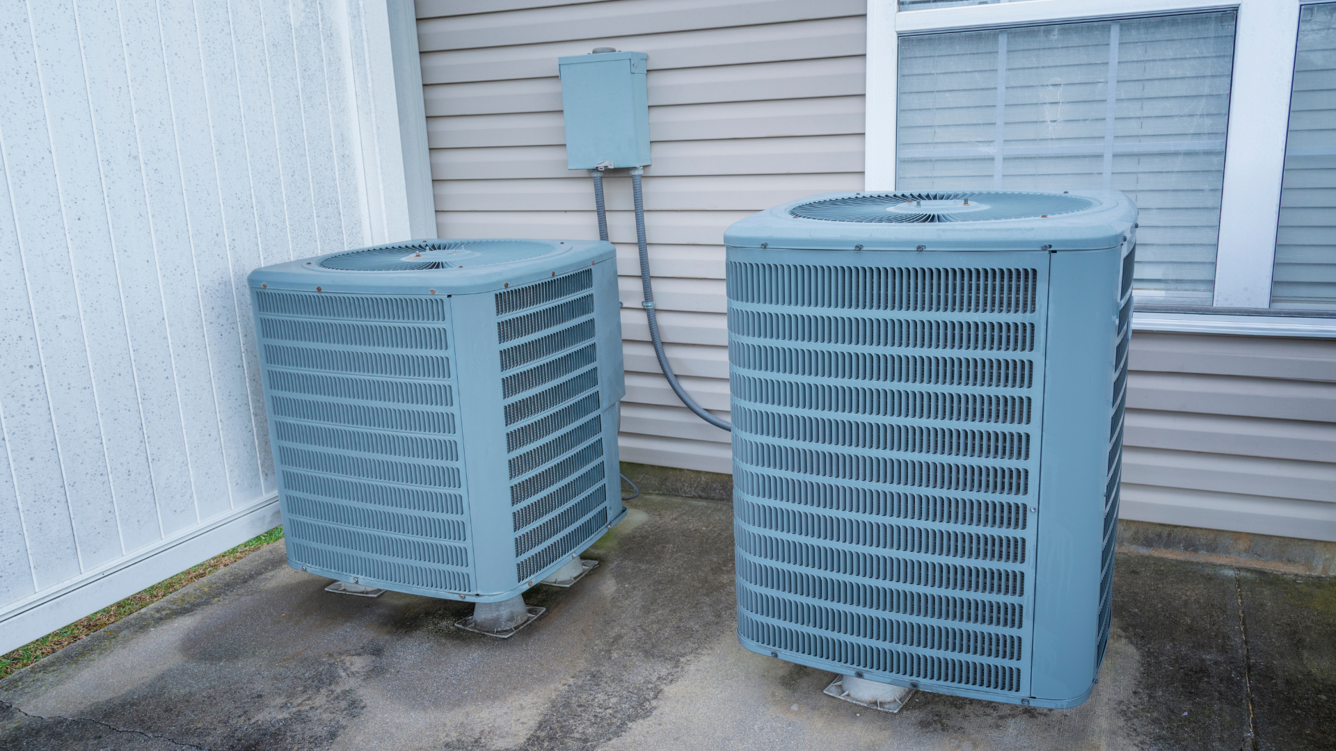two air conditioners are sitting outside of a house .