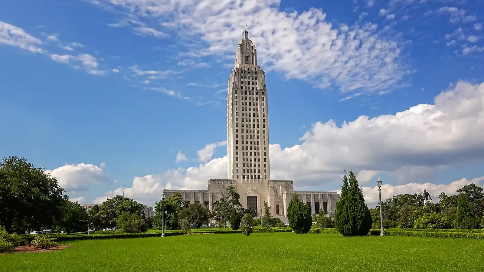 The louisiana state capitol building is surrounded by green grass and trees.