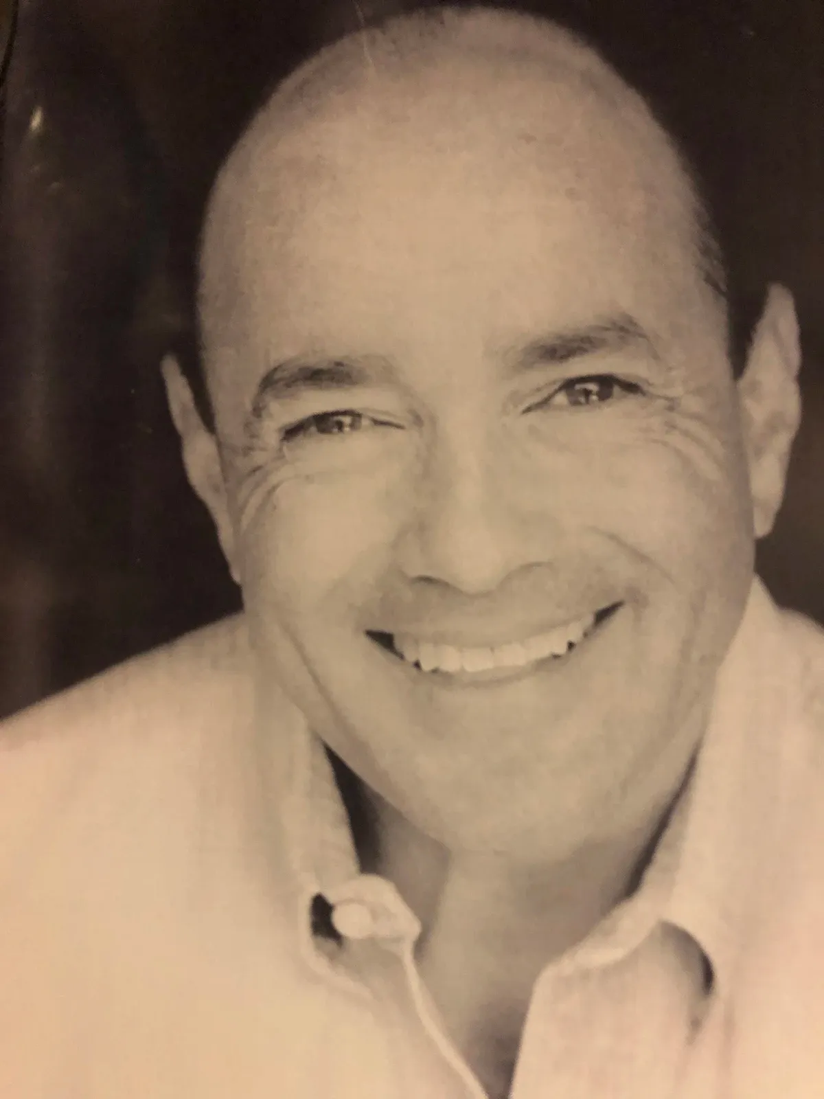 A bald man is smiling in a black and white photo.