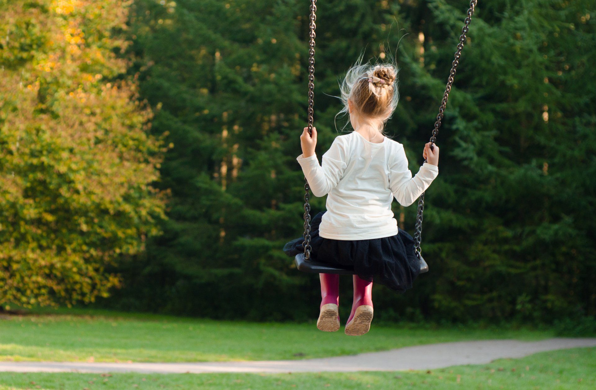 A little girl is sitting on a swing in a park.