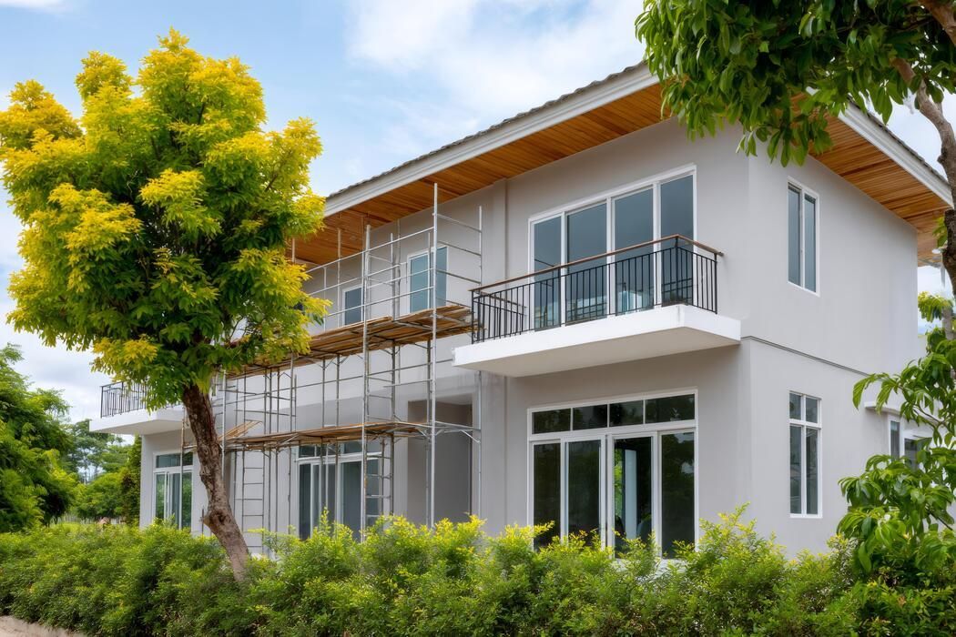 Modern two-story white house with balcony, surrounded by lush green trees and garden
