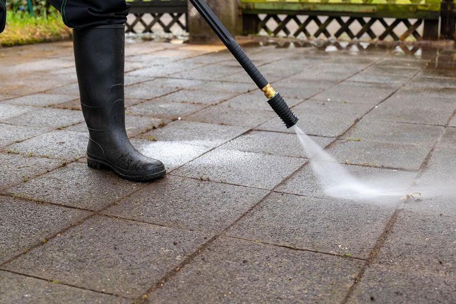 Person pressure-washing wet stone pavement with a wand while wearing black boots