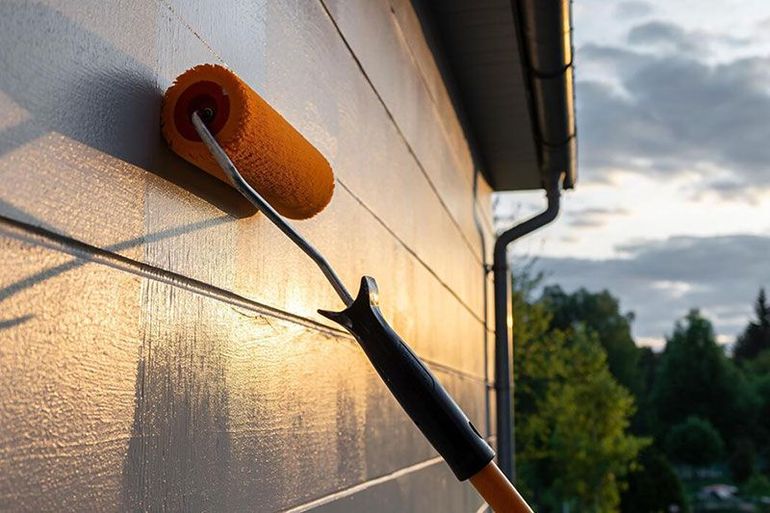 Paint roller applying orange paint to a house exterior at sunset