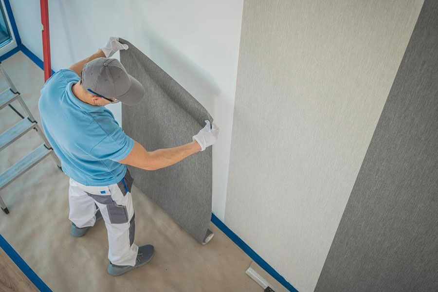 Worker installing gray wall panel in a room with blue painter’s tape along the floor and walls