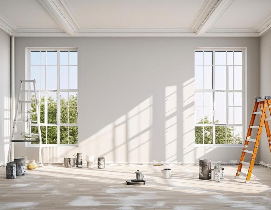Bright empty room under renovation with white walls, large windows, sunlight, paint cans, and a ladder