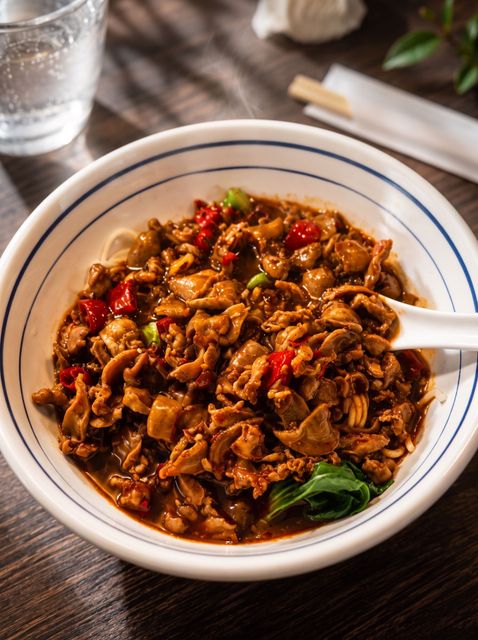 Bowl of spicy stir-fried noodles with vegetables on a wooden table