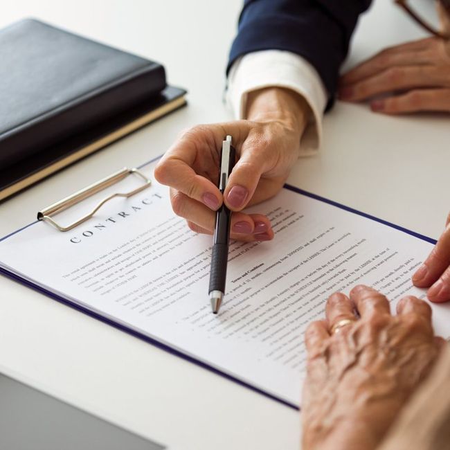 Hands signing a contract on a clipboard with a pen at a white desk