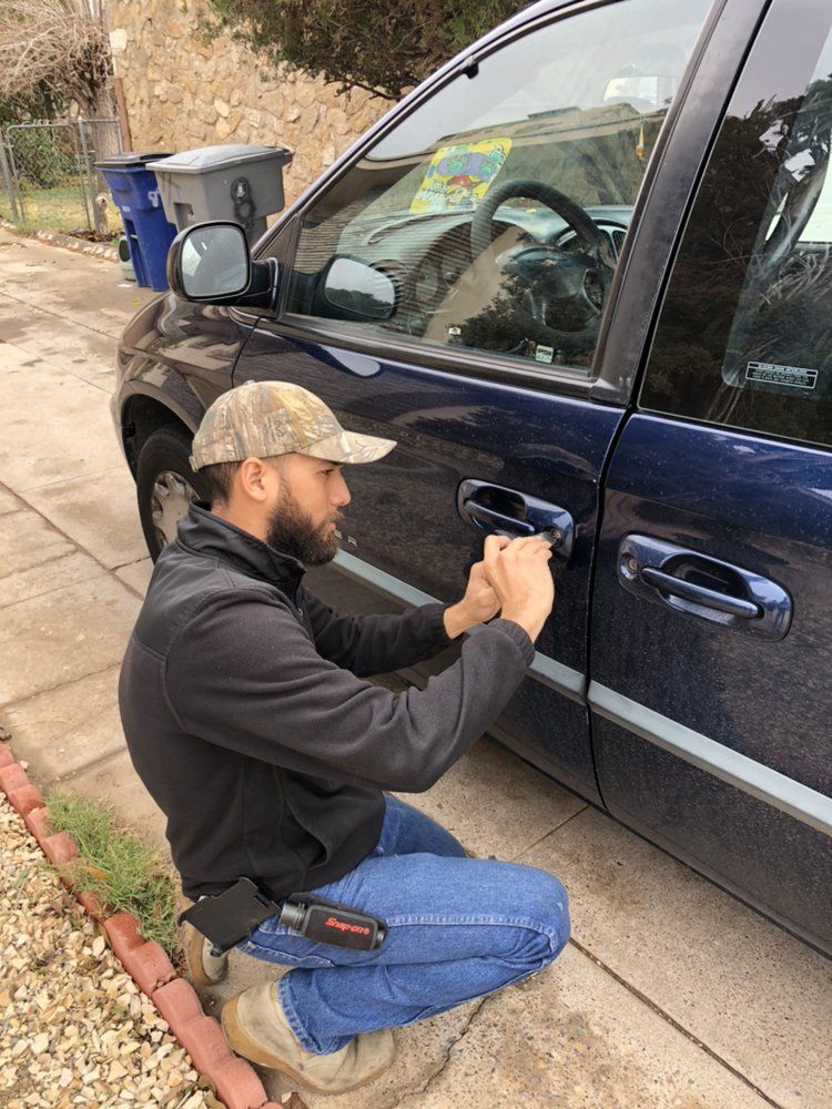 Locks Keys and More | A man is kneeling down next to a blue car.