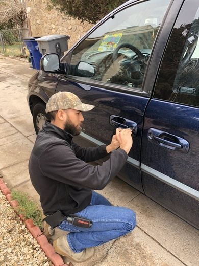 Locks Keys and More | A man is kneeling down next to a blue car.