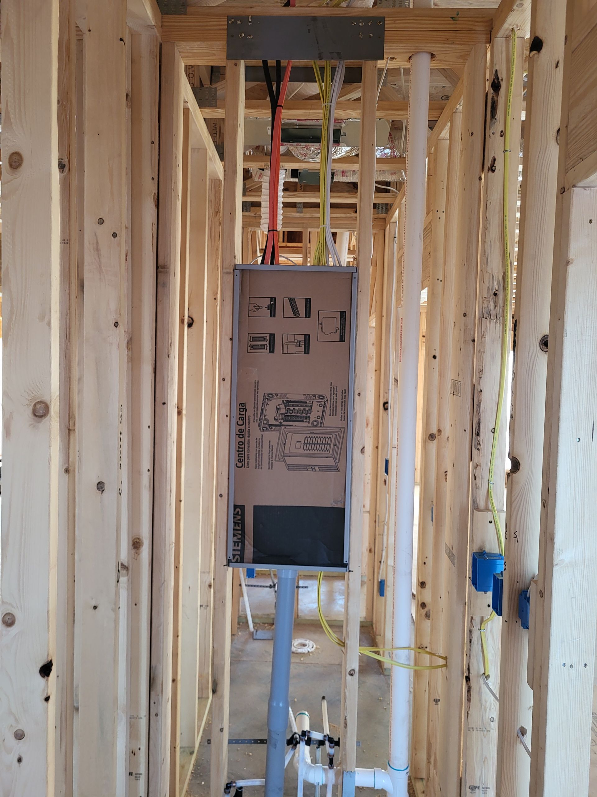 Interior view of a building frame with a panel box, plumbing, and electrical wiring.
