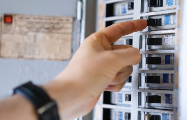 Hand flipping a circuit breaker switch in a gray electrical panel.