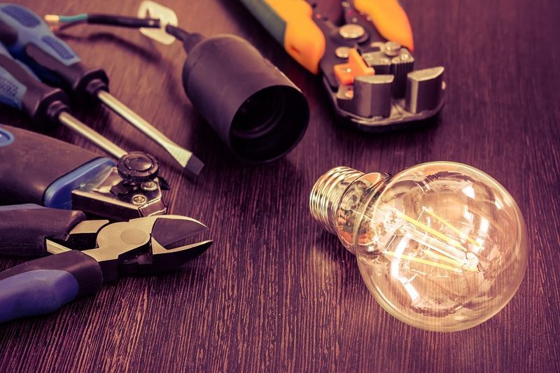 Tools and lightbulb on a dark wood surface, including screwdrivers, wire strippers, and a bulb holder.