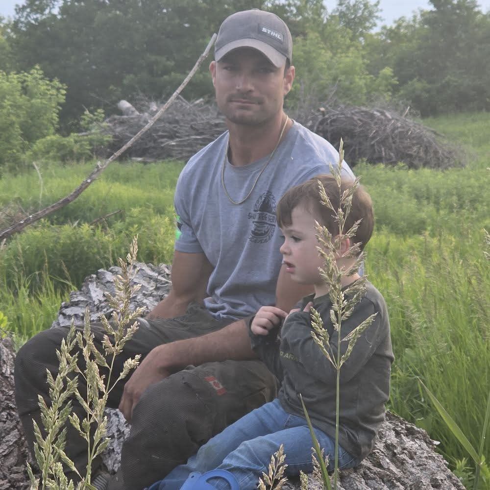 A man and a child are sitting on a log in a field