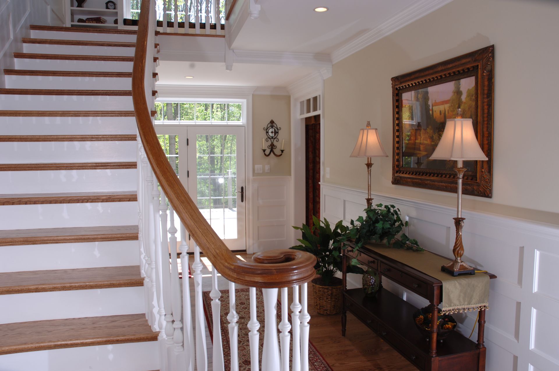 A hallway with stairs and a table with lamps on it