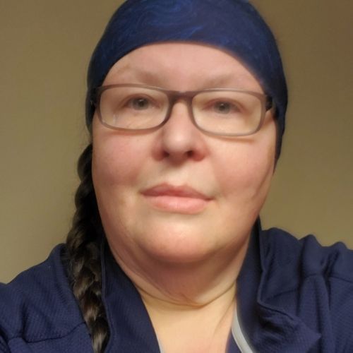 Person wearing glasses and a blue headscarf, looking at the camera against a plain beige background.