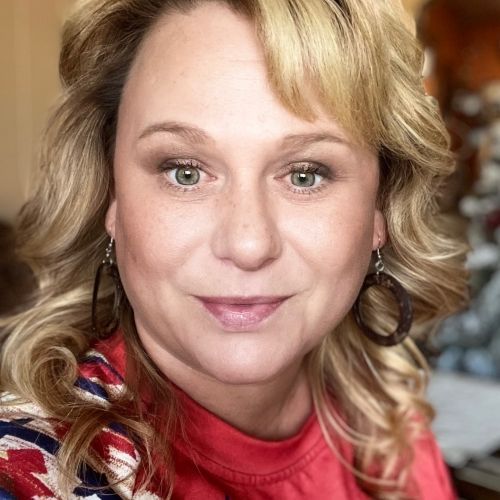 Close-up of a smiling woman with blonde curls wearing a red top and star-spangled scarf