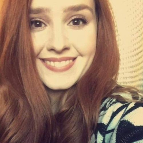 Smiling woman with long red hair in a patterned sweater, close-up portrait against a neutral background