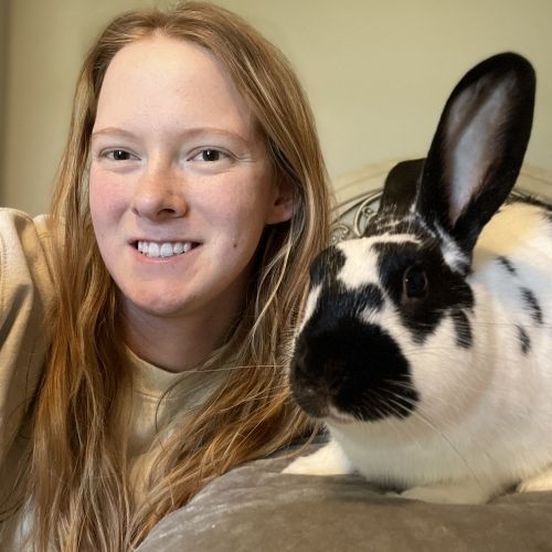 Woman smiling beside a black-and-white rabbit with one upright ear