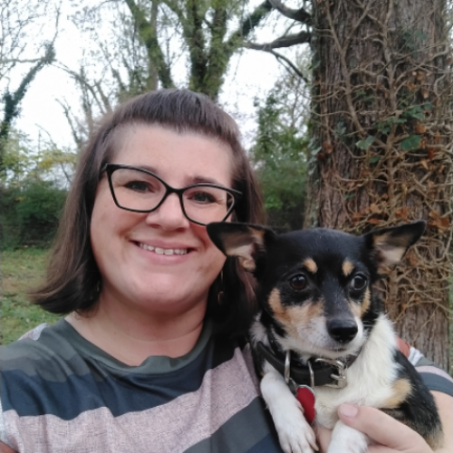 Smiling person holding a small black-and-tan dog outdoors by a tree