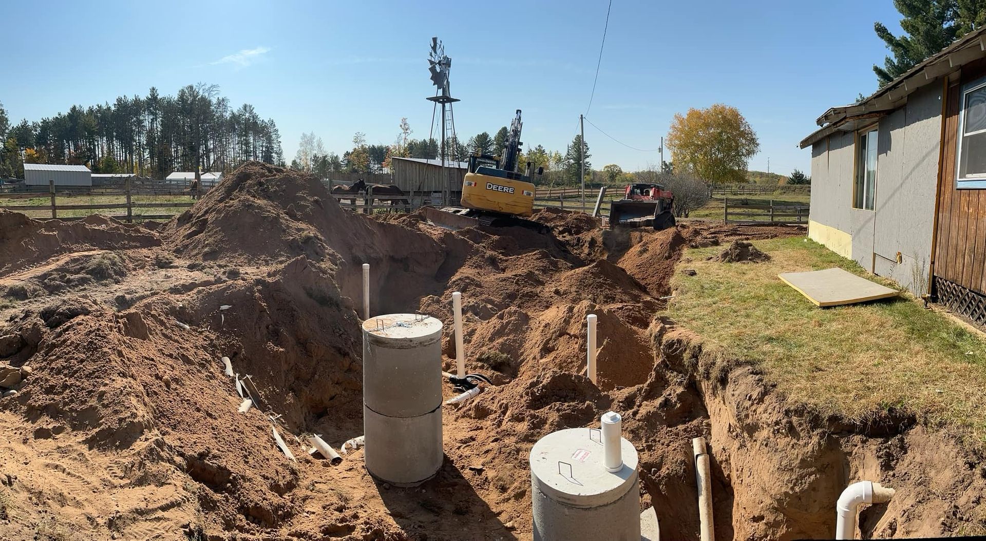Construction equipment excavating a yard for a residential septic system installation featuring two concrete tanks.